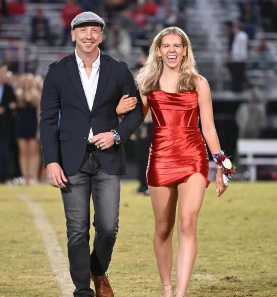 Brad Shortridge, smiling in a flat cap and blazer, walking arm in arm with his daughter across a football field.